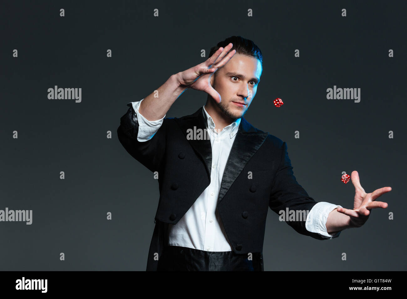 Handsome young man magician showing tricks with flying dice over grey background Stock Photo