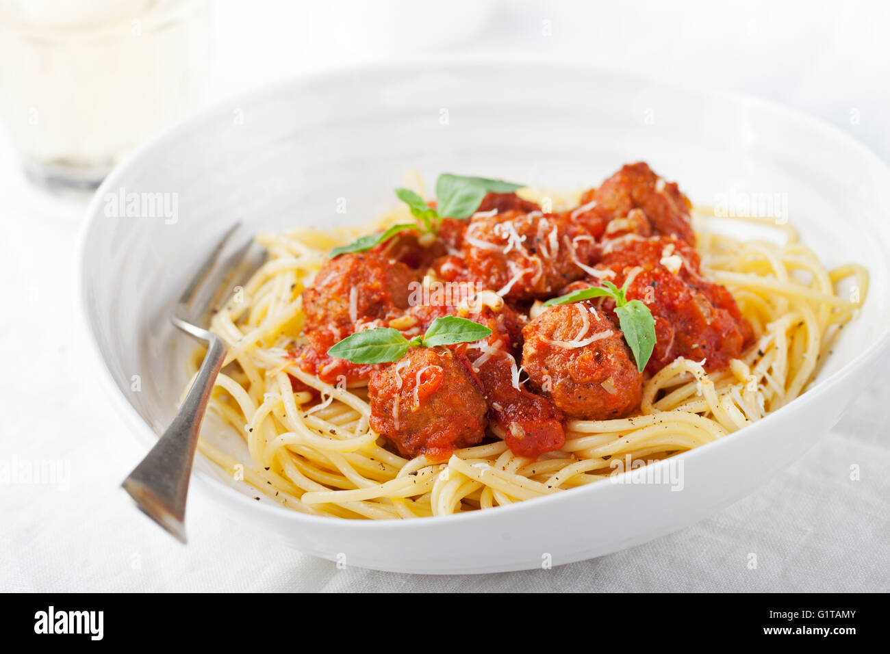 Meatballs in tomato sauce and fresh basil with spaghetti on a white