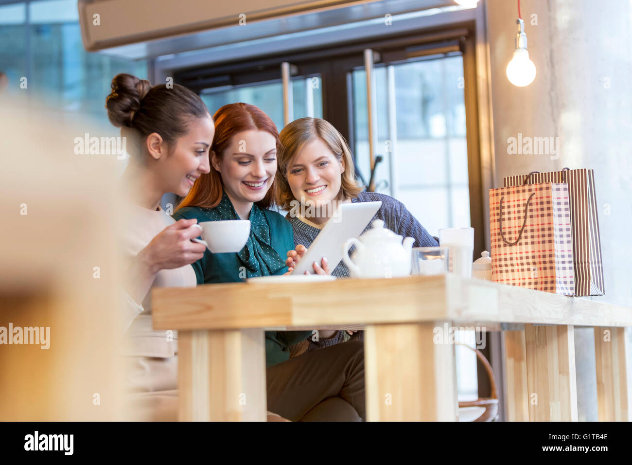 Smiling women drinking tea and sharing digital tablet at cafe counter Stock Photo