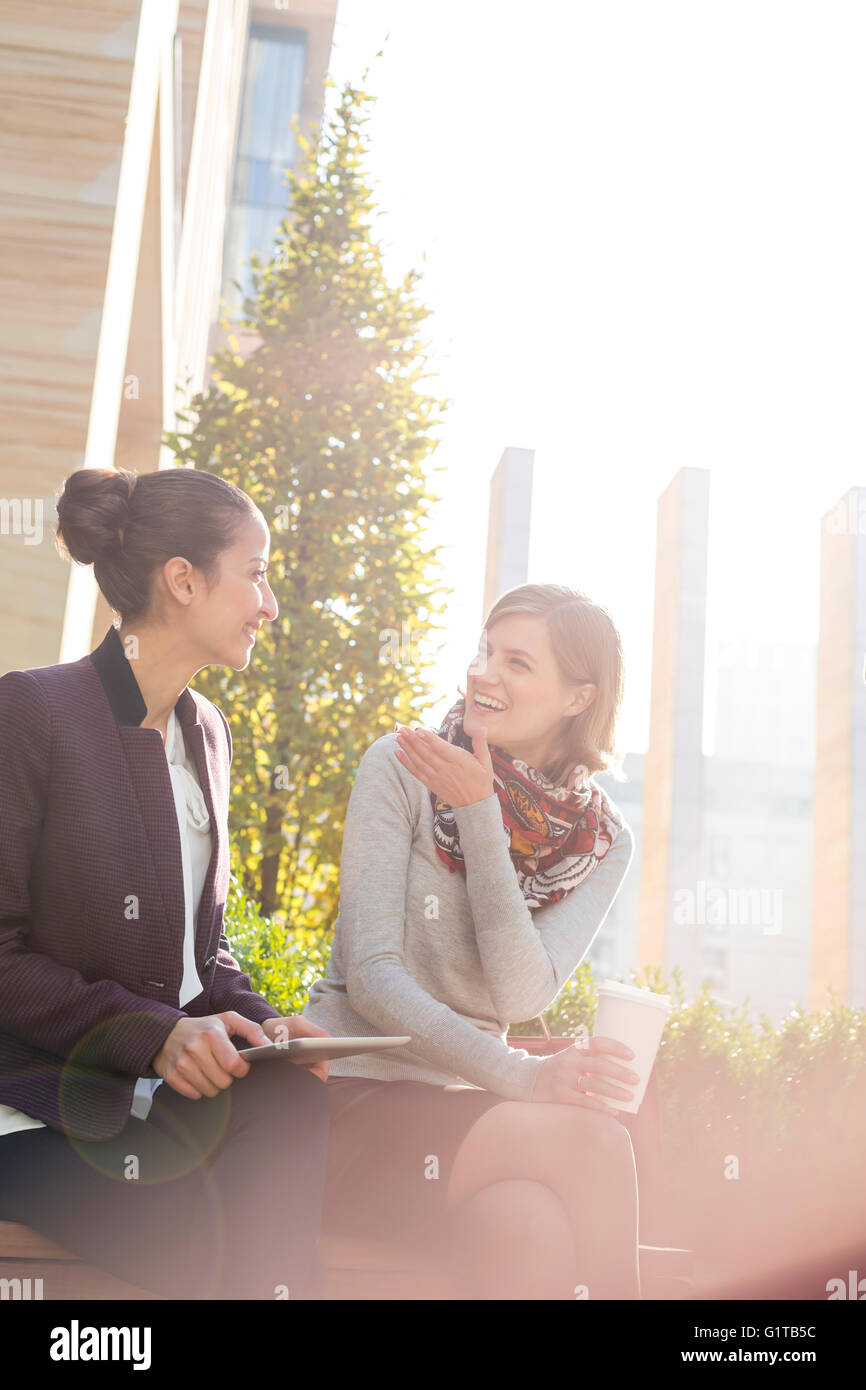 Smiling businesswomen with digital tablet and coffee talking in city park Stock Photo