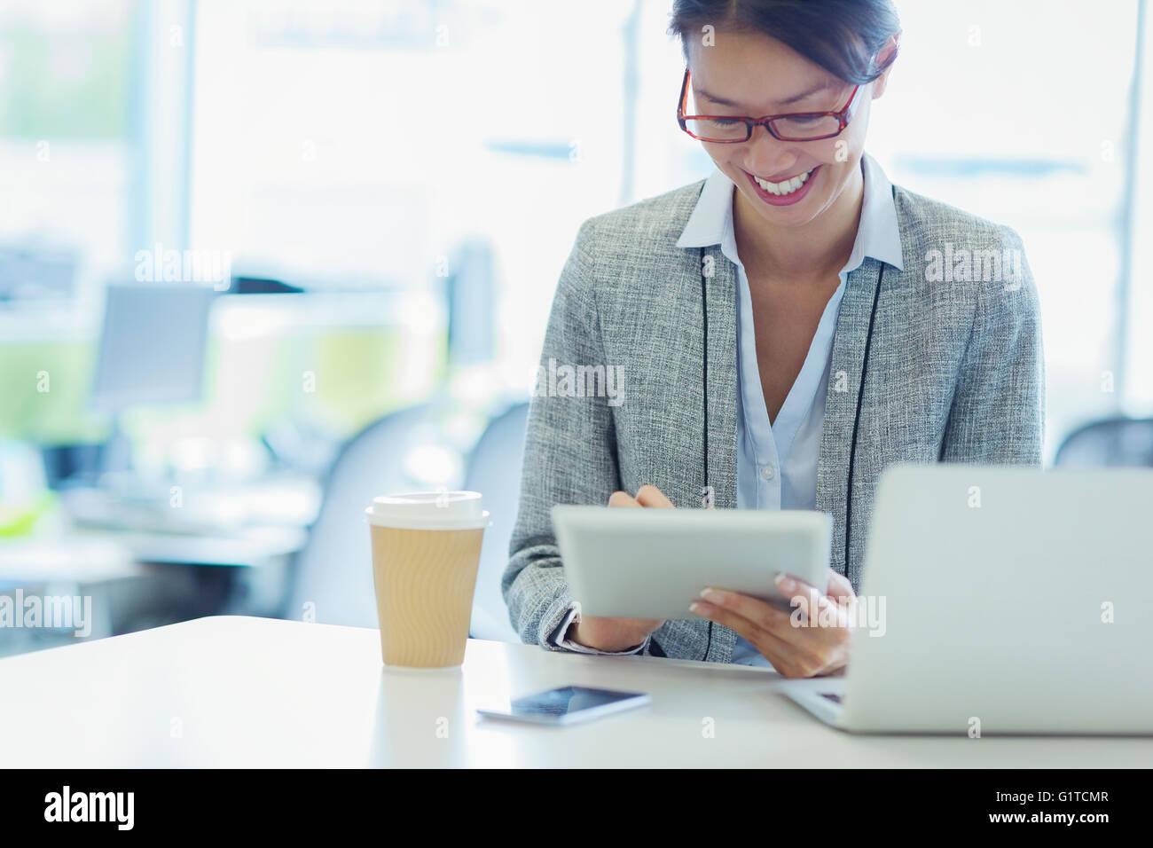 Smiling businesswoman using digital tablet with coffee in office Stock Photo