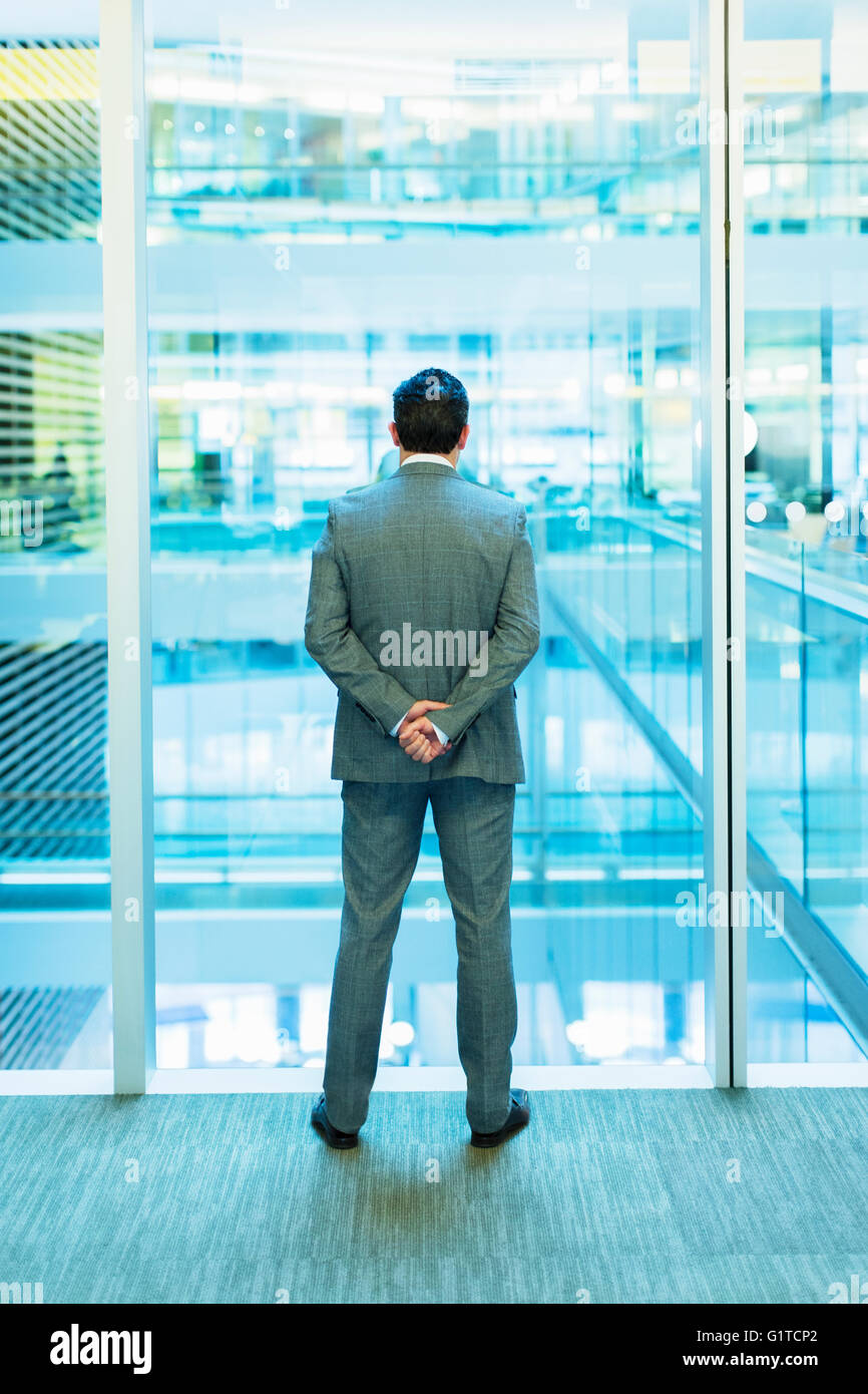 Businessman standing at atrium window with hands behind back Stock Photo
