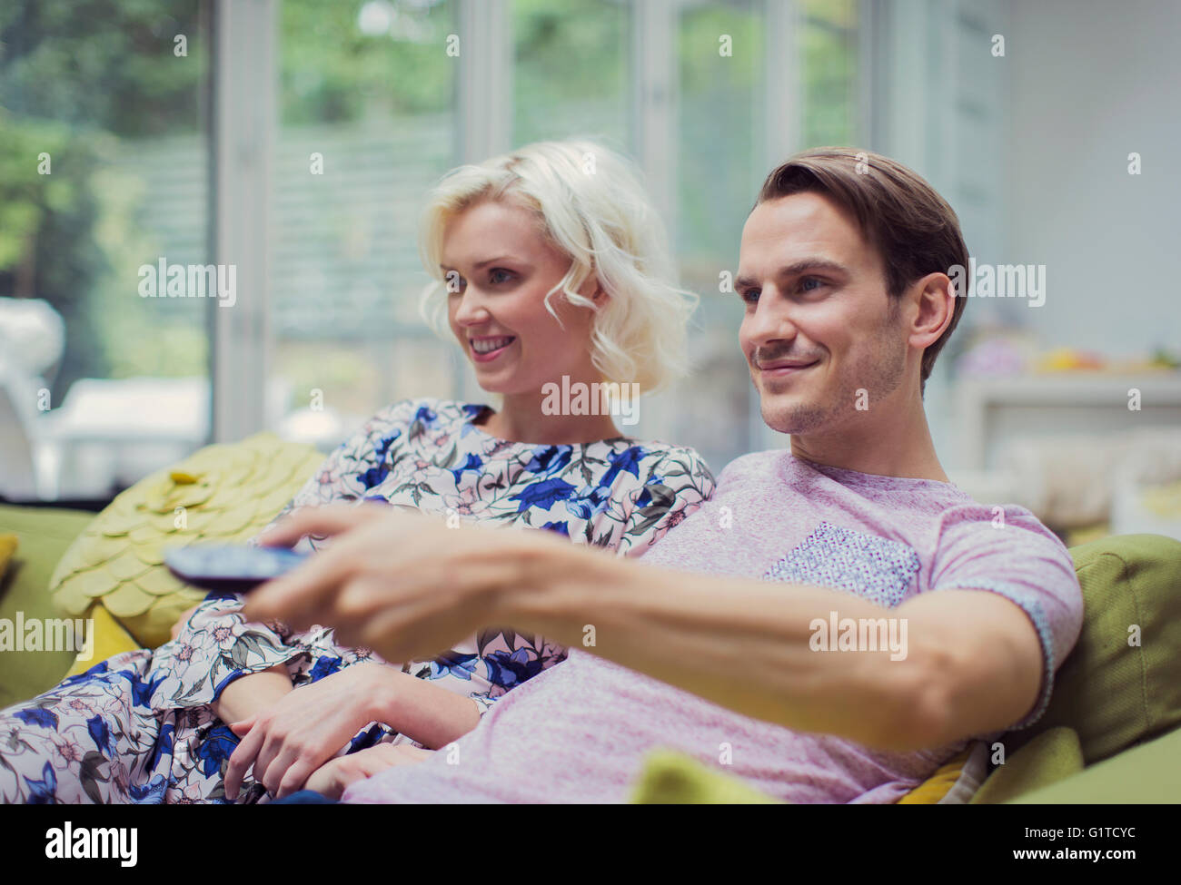 Smiling couple watching TV in living room changing channels Stock Photo