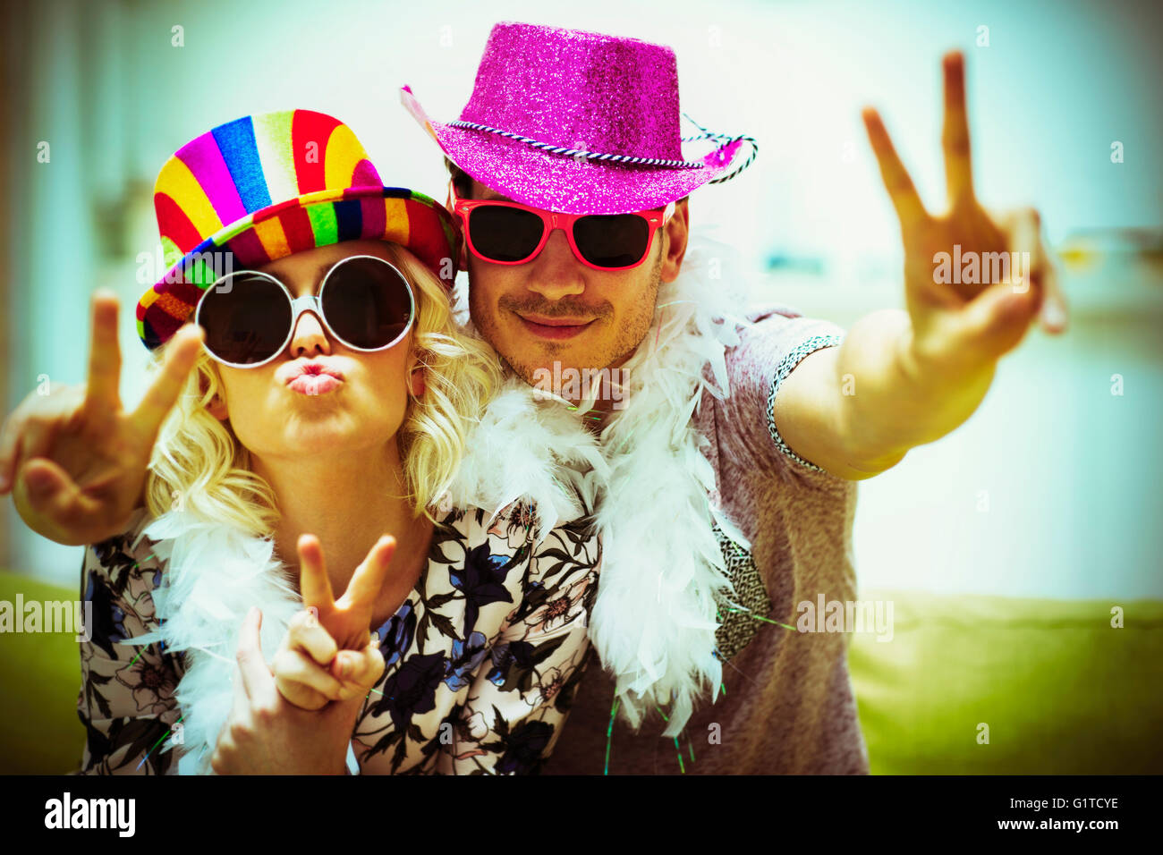 Portrait playful couple in costume sunglasses and hats gesturing peace sign Stock Photo