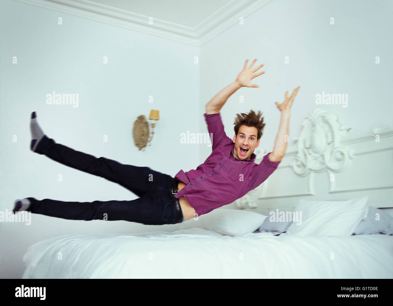 Portrait playful man jumping onto bed Stock Photo
