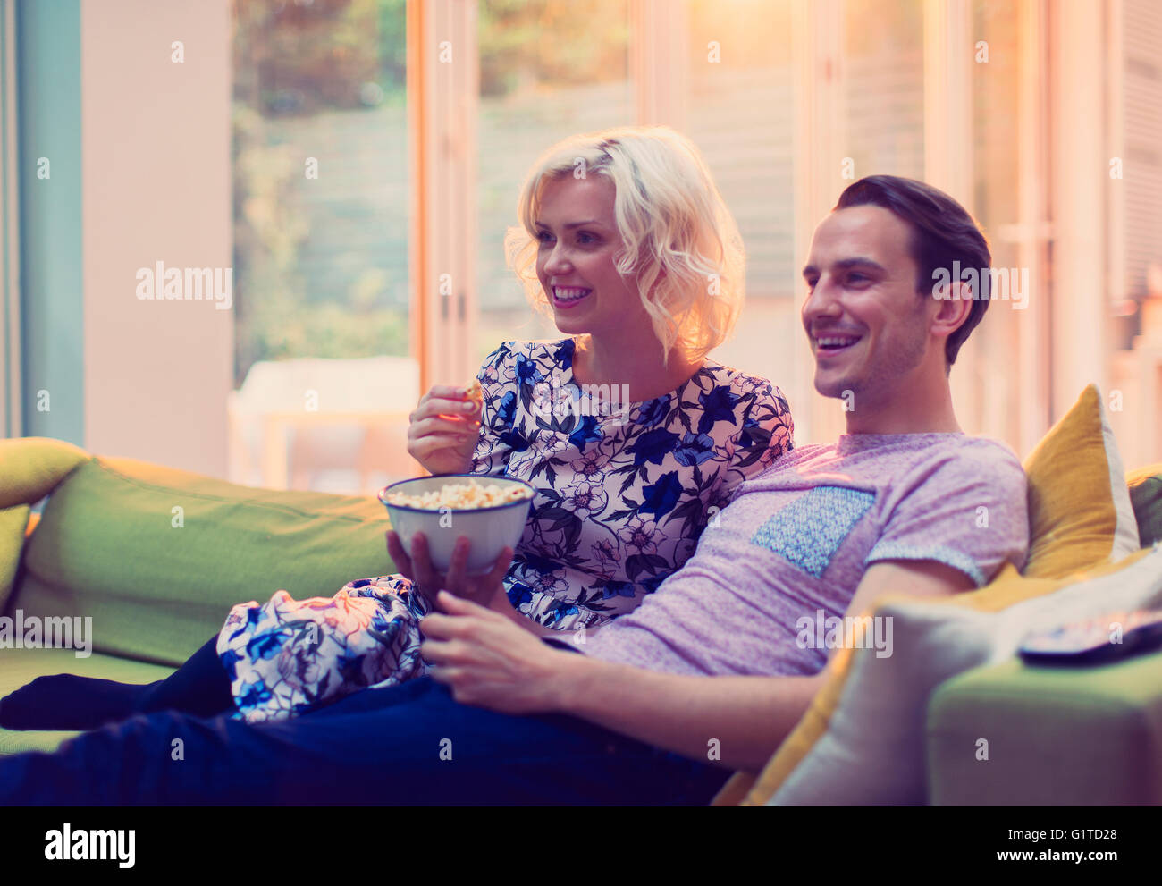 Couple watching TV and eating popcorn on living room sofa Stock Photo