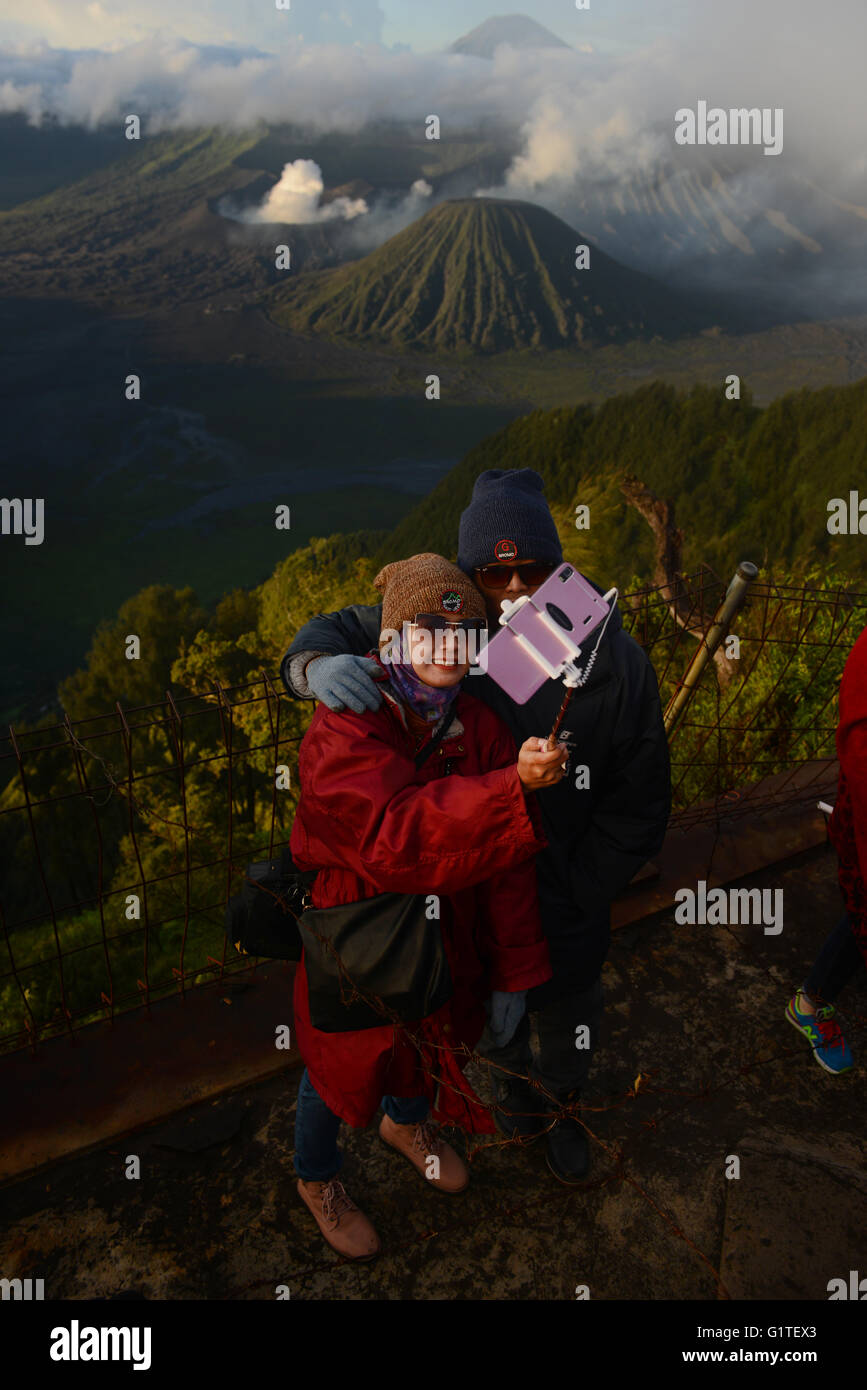A couple taking a selfie with their smartphone and selfie stick in front of Bromo-Batok-Semeru volcanoes in Java, Indonesia. Stock Photo
