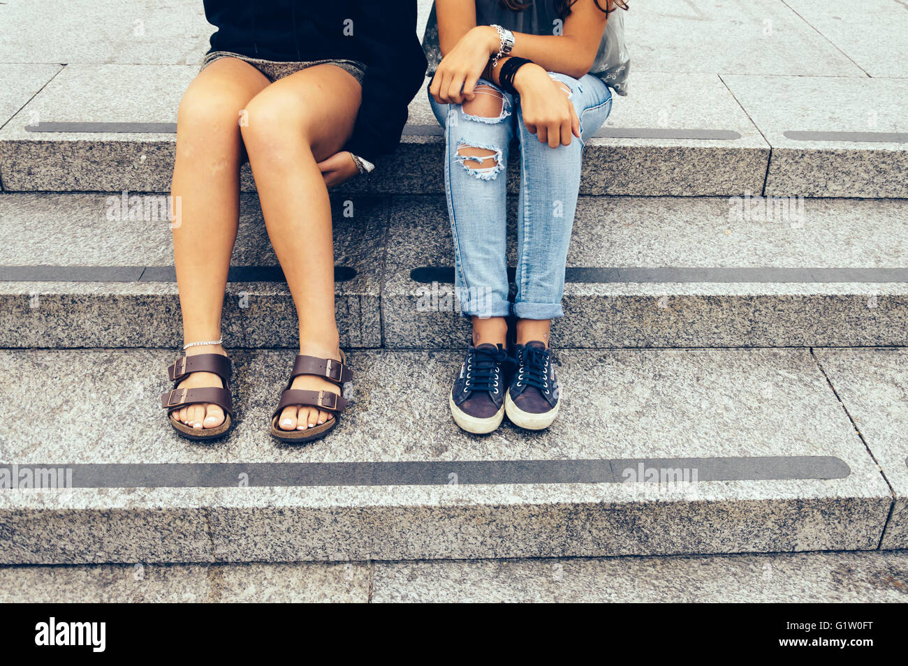 Two young women sitting in the city, one of them wear denim broken jeans and the other shorts. Only legs showing Stock Photo