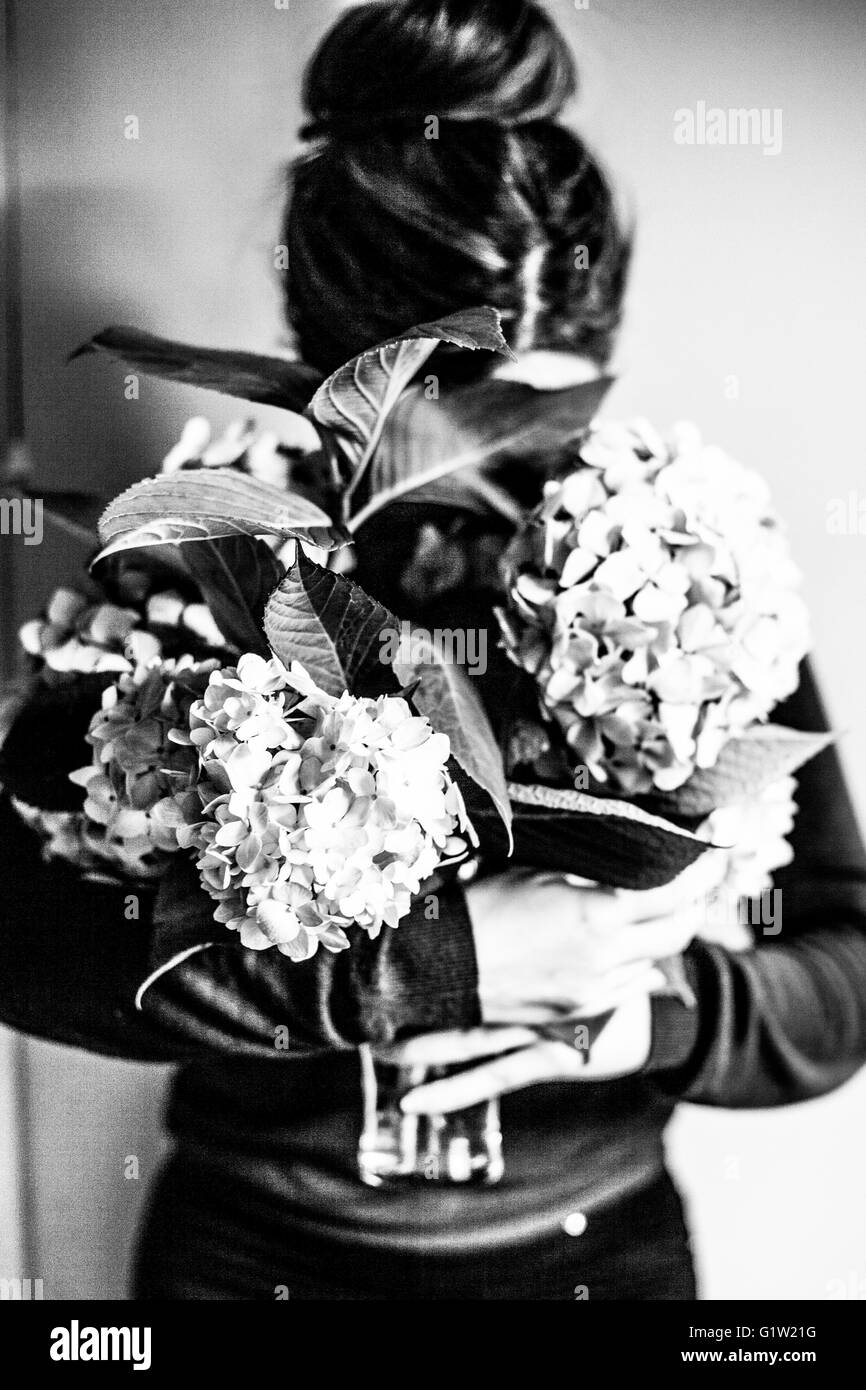 Black and white image of a woman with hair tied up in a bun with hydrangeas Stock Photo