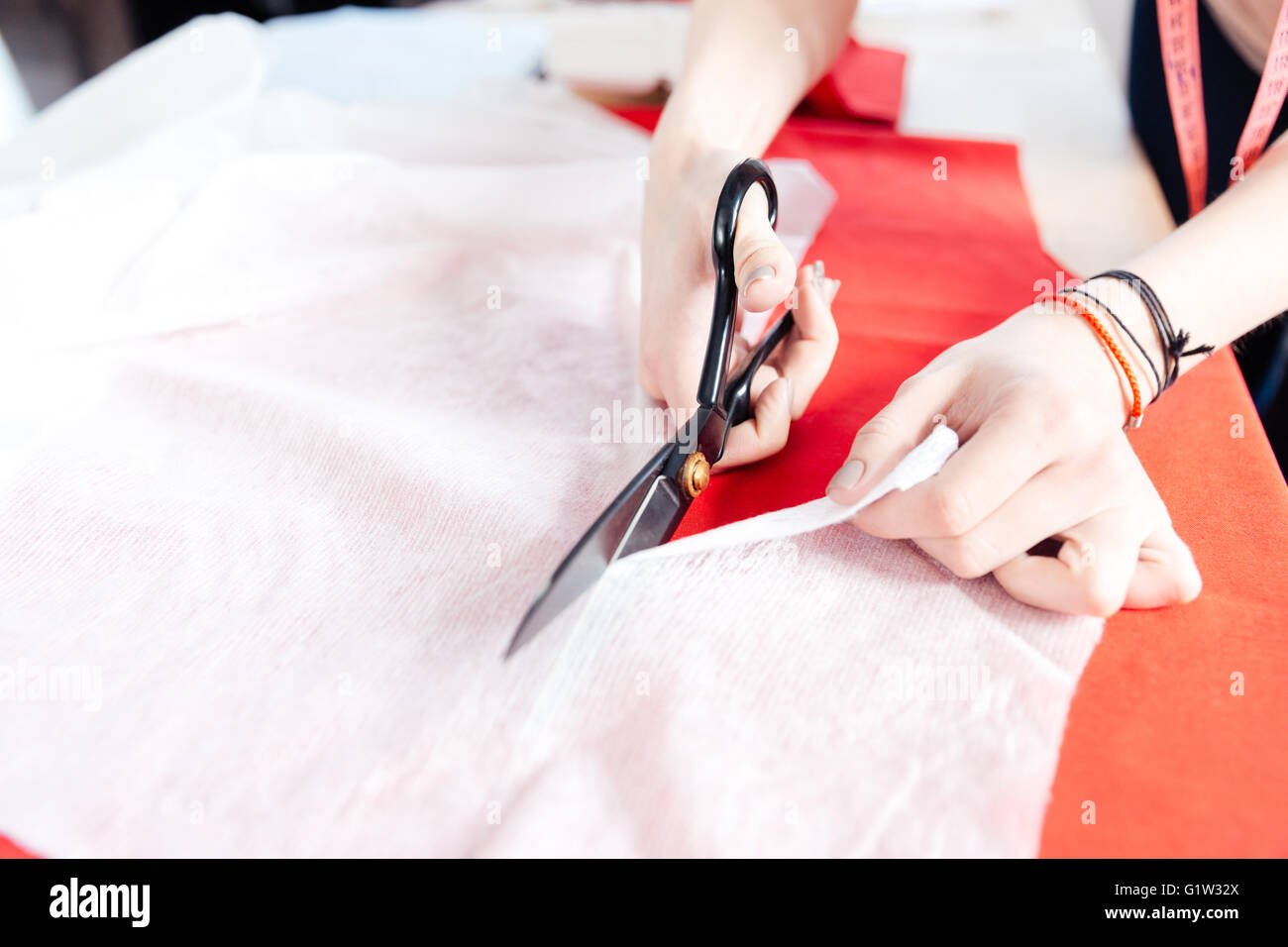 Hands of young woman seamstress with scissors cutting white fabric Stock Photo