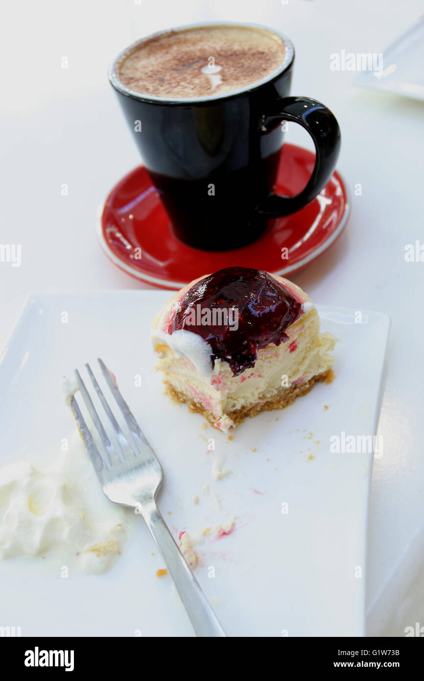 Half eaten strawberry cheesecake and a cup of coffee on white table Stock Photo