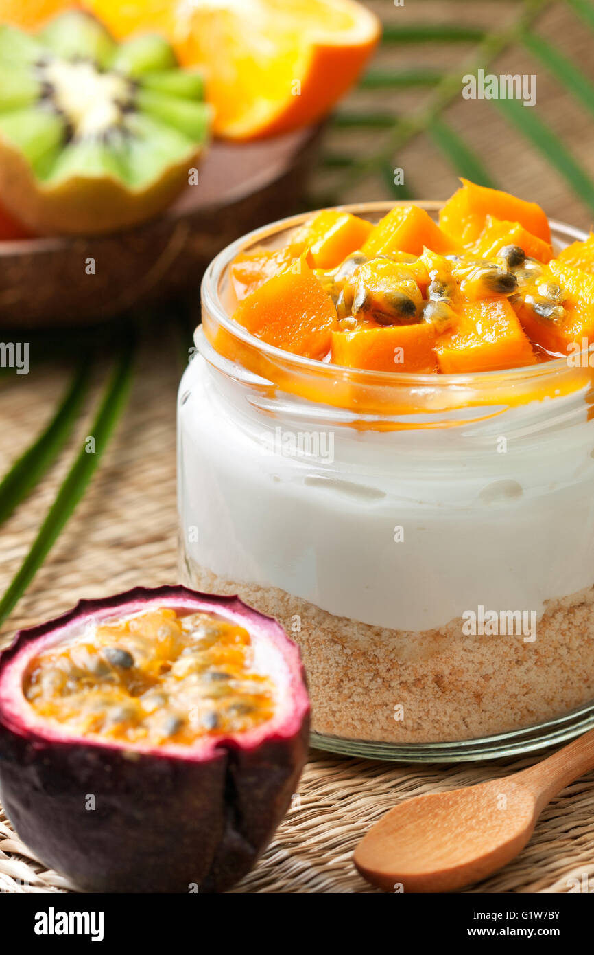 cheesecake in a jar with tropical fruits: mango, passionfruit. kiwi slices, orange and passionfruit on straw background Stock Photo