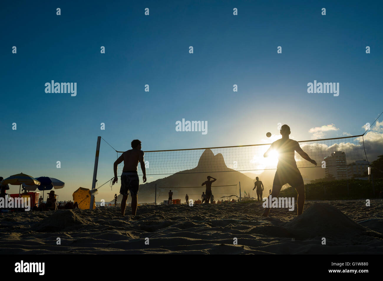 Silhouettes of Brazilians playing futevolei (footvolley) against a sunset on Dois Irmaos Two Brothers Mountain on Ipanema Beach Stock Photo