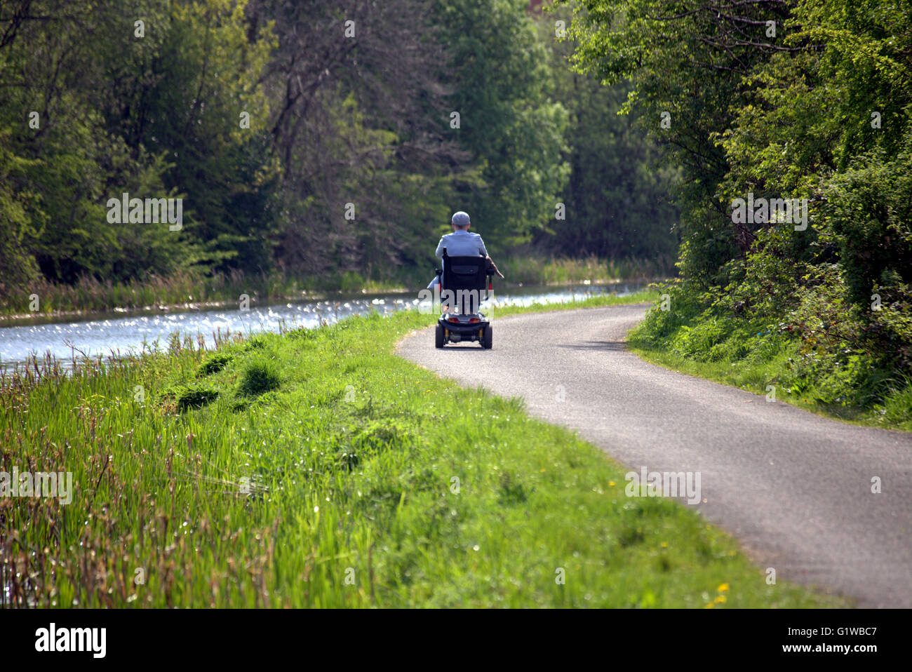 Man on invalid car  on towpath on the Forth and Clyde canal, Glasgow, Scotland, UK. Stock Photo