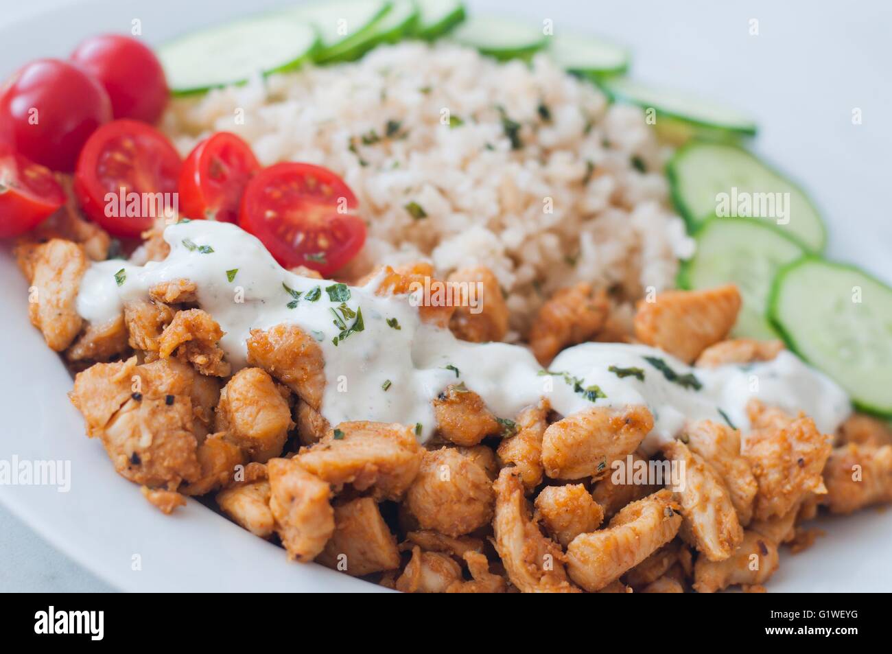 Gyros chicken on a plate with rice, tzatziki dressing and vegetables -  tomato, cucumber Stock Photo - Alamy