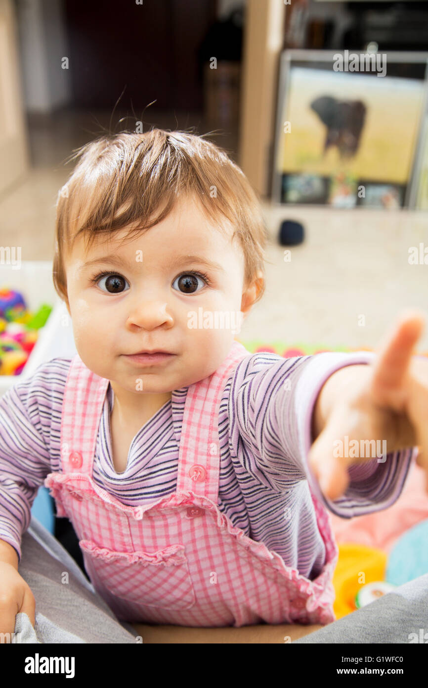 Cute little one year old kid with wide open eyes looking at camera and pointing at it Stock Photo