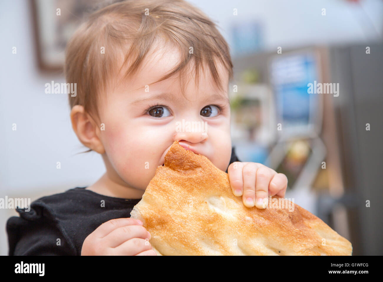 Close-up of lovely one year old baby biting a large piece bread Stock Photo
