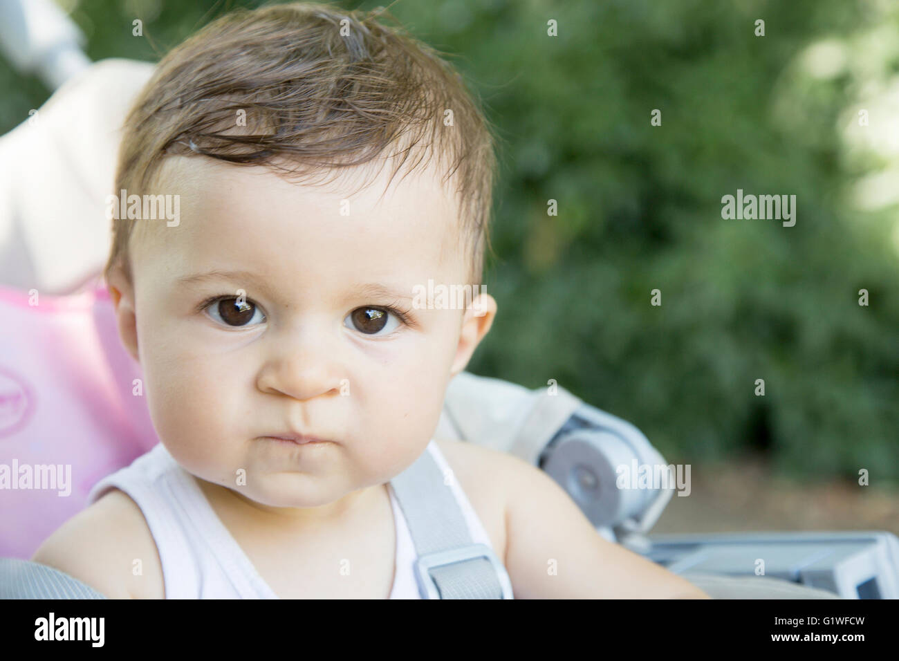 One year old baby looking angrily at camera while sitting against of green background Stock Photo