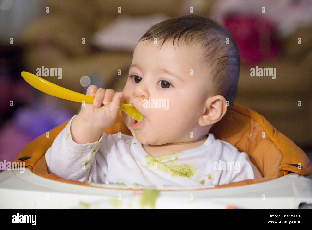 Cute six months old baby eating with spoon with very dirty clothes
