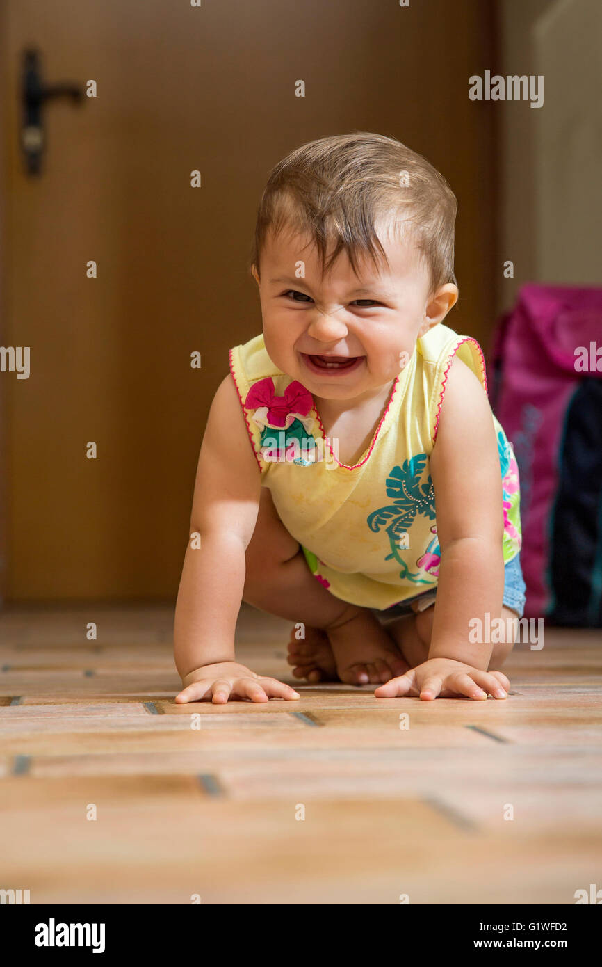 Portrait of happy laughing one year old kid crawling on floor and looking at camera Stock Photo