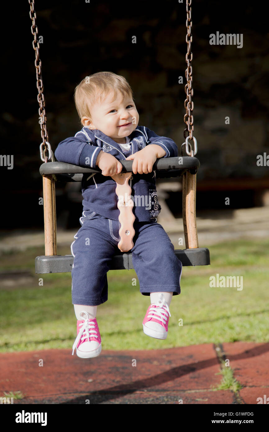 Lovely smiling one year old kid sitting on swing and looking at camera Stock Photo
