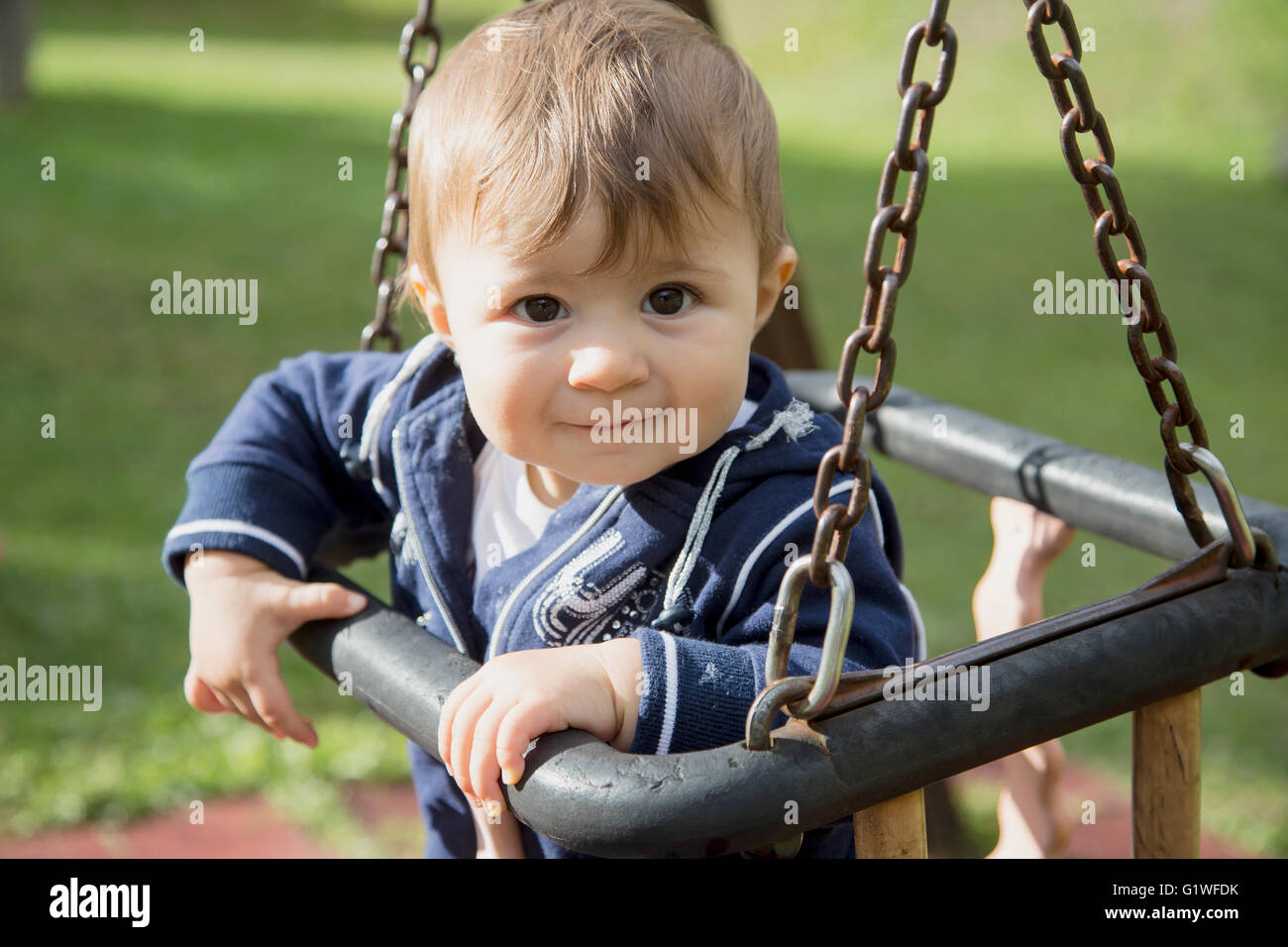 Portrait of lovely one year old baby girl sitting on swings at playground Stock Photo
