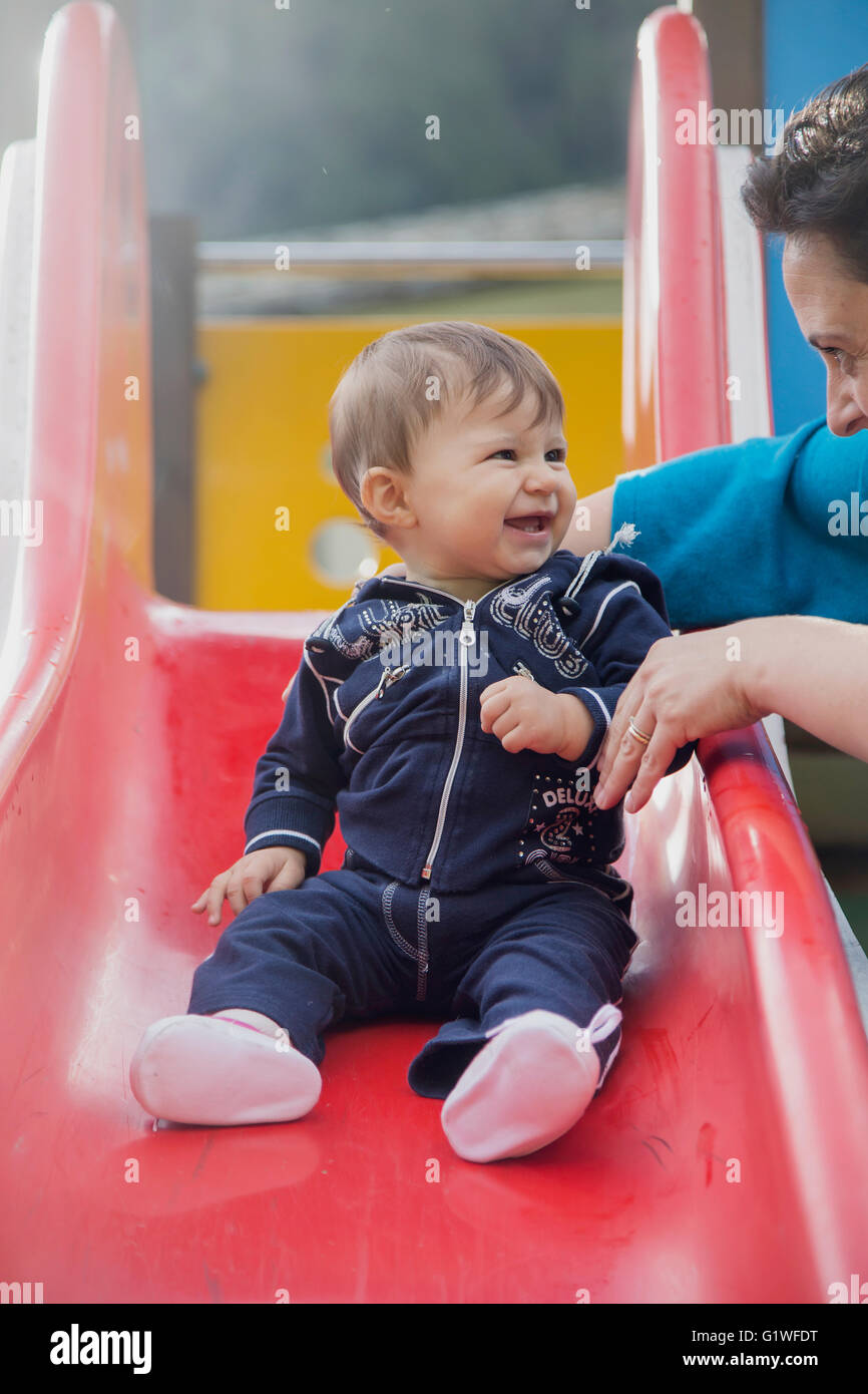 Portrait of smiling lovely one year old baby on plastic slide looking at mother Stock Photo
