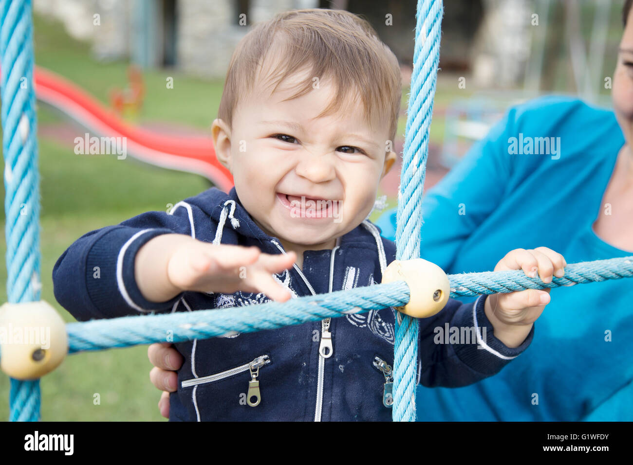 Portrait of happy one year old baby looking at camera while holding on blue ropes Stock Photo