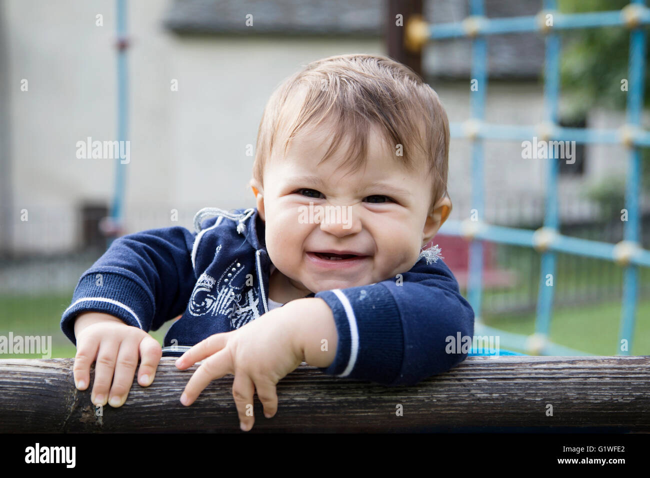 One year old baby girl climbing a wooden fence in a playground Stock Photo
