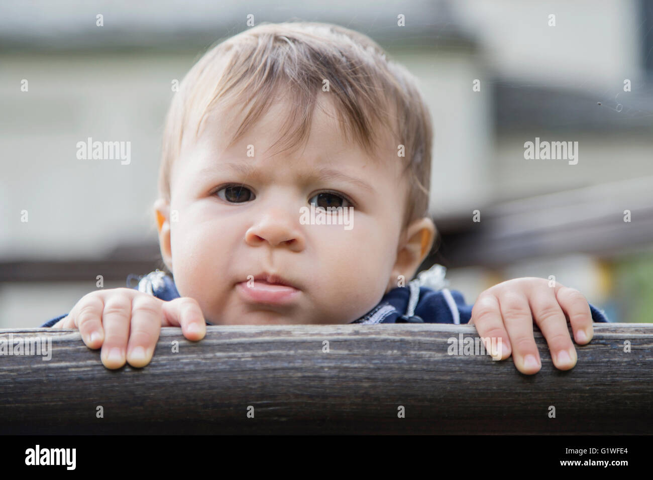 Portrait of one year old baby looking at camera seriously while holding hands on wooden fence Stock Photo