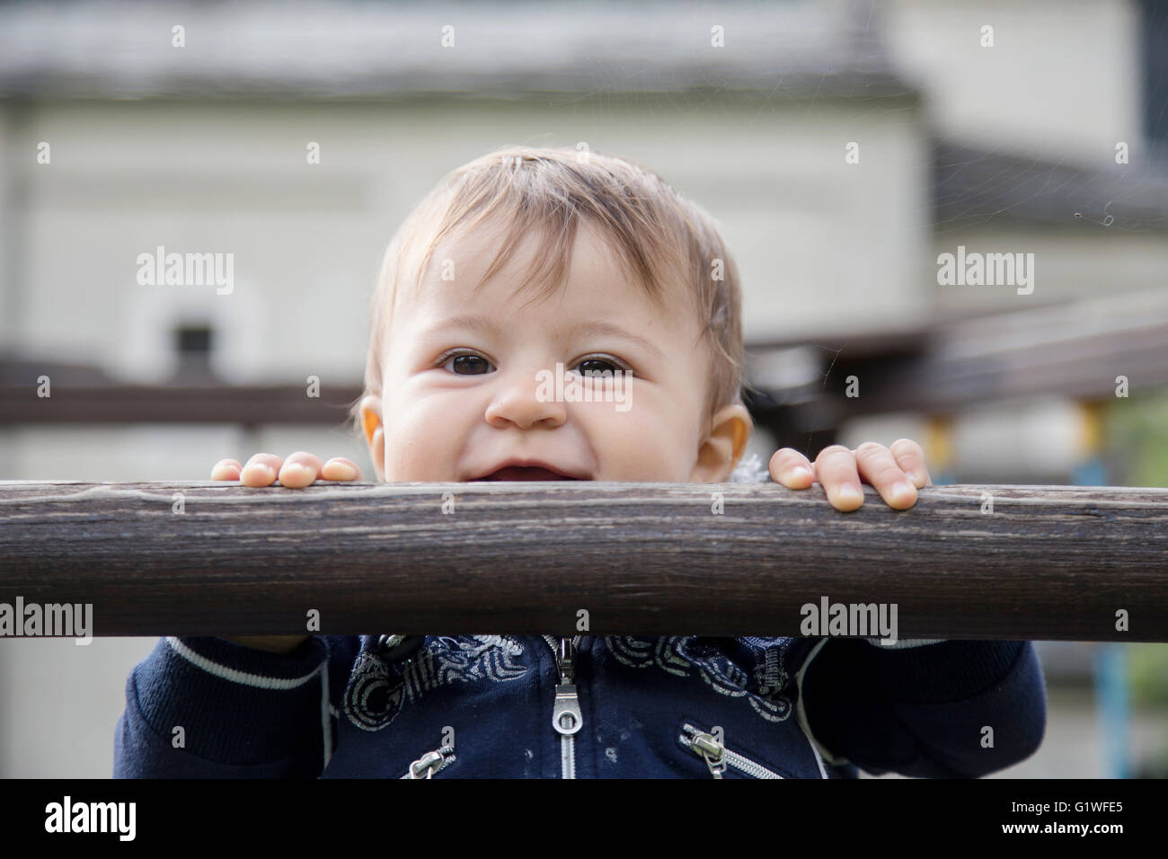 Portrait of smiling one year old kid hanging on wooden bar and looking at camera Stock Photo