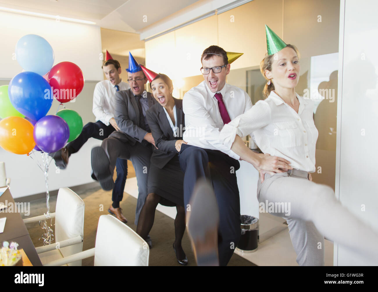 Playful business people with party hats dancing in conga line Stock Photo