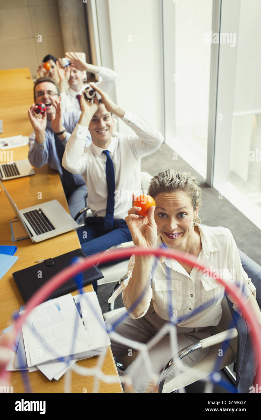 Business people aiming plastic balls at basketball hoop in conference room Stock Photo