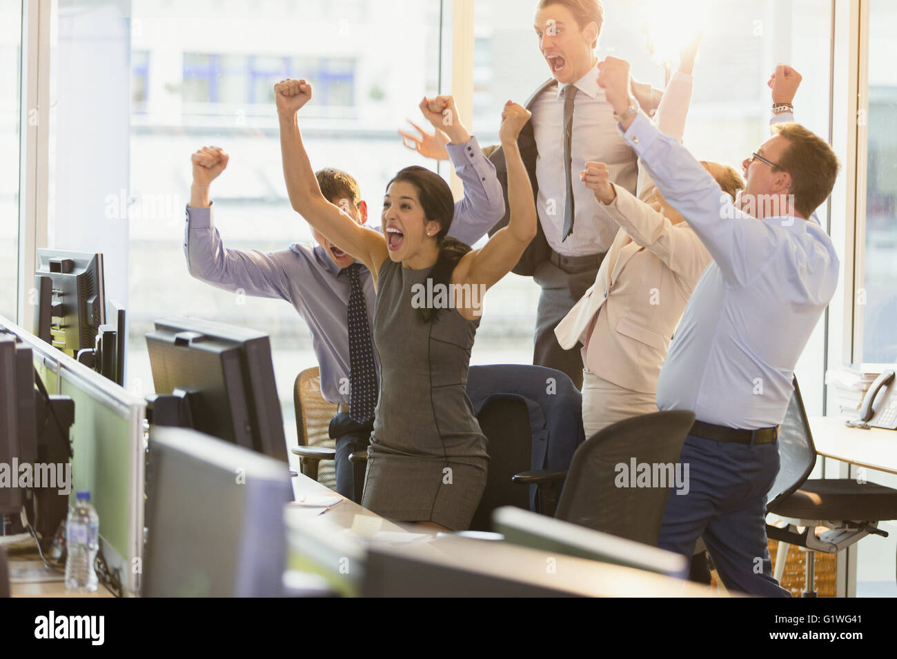 Exuberant business people cheering with arms raised in office Stock Photo