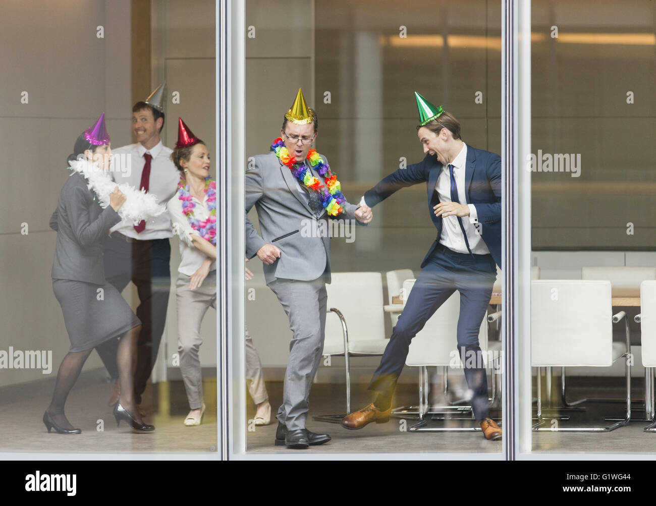Playful business people in party hats dancing at conference room window Stock Photo