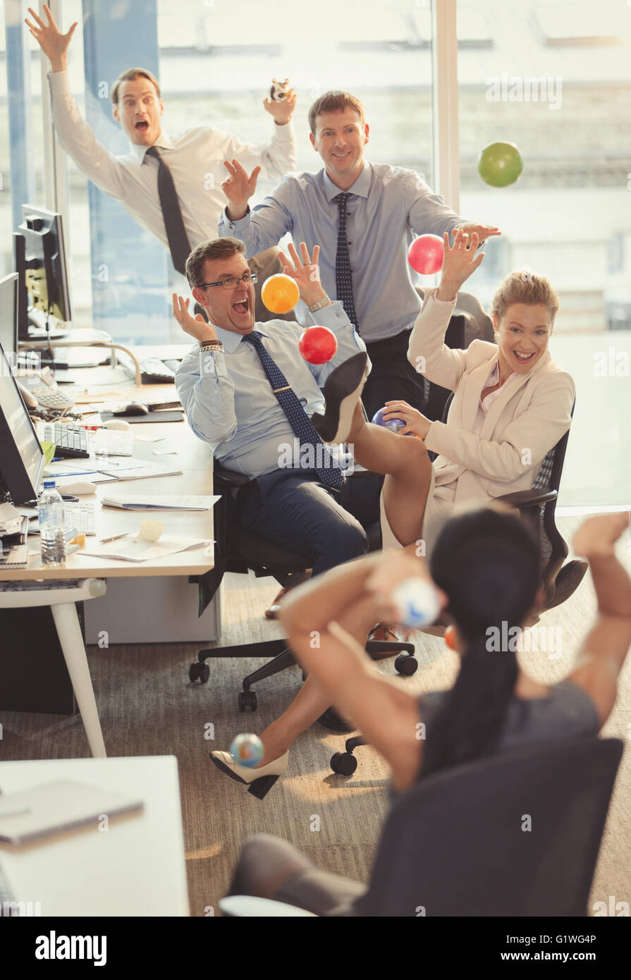 Playful business people throwing colorful plastic balls at each other ...