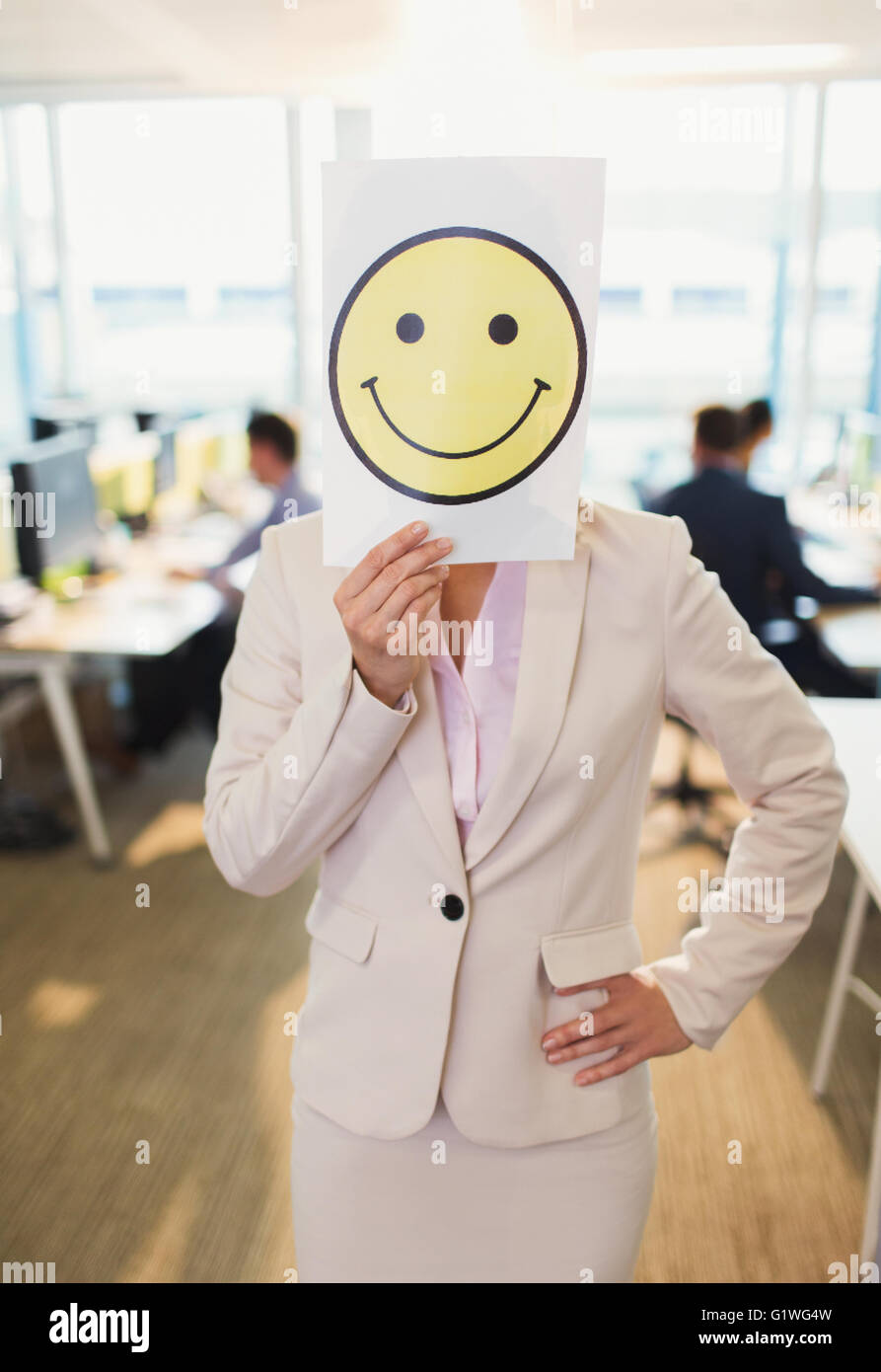 Portrait of businesswoman holding smiley face printout over her face in office Stock Photo