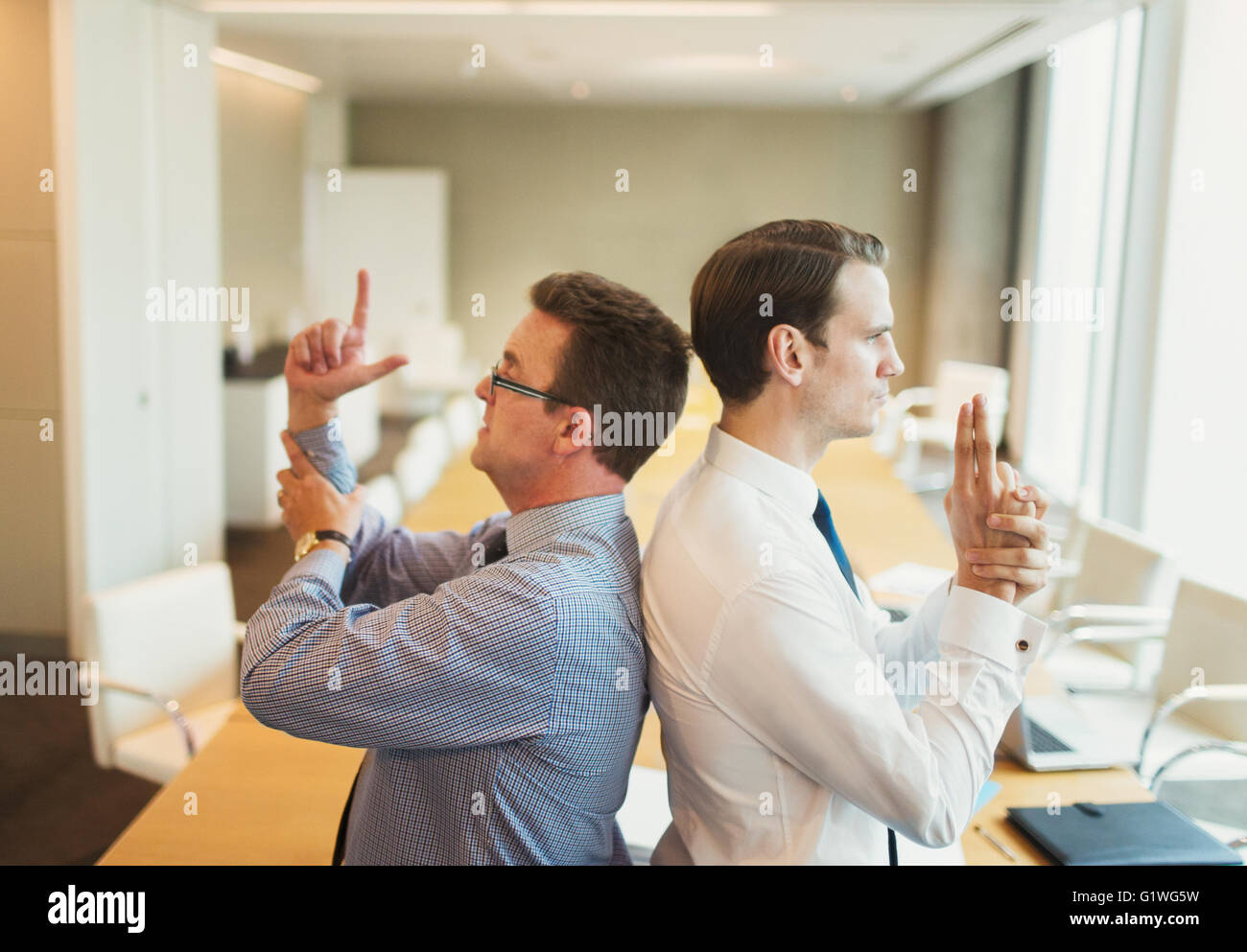 Playful businessmen pretending to duel back to back in conference room Stock Photo