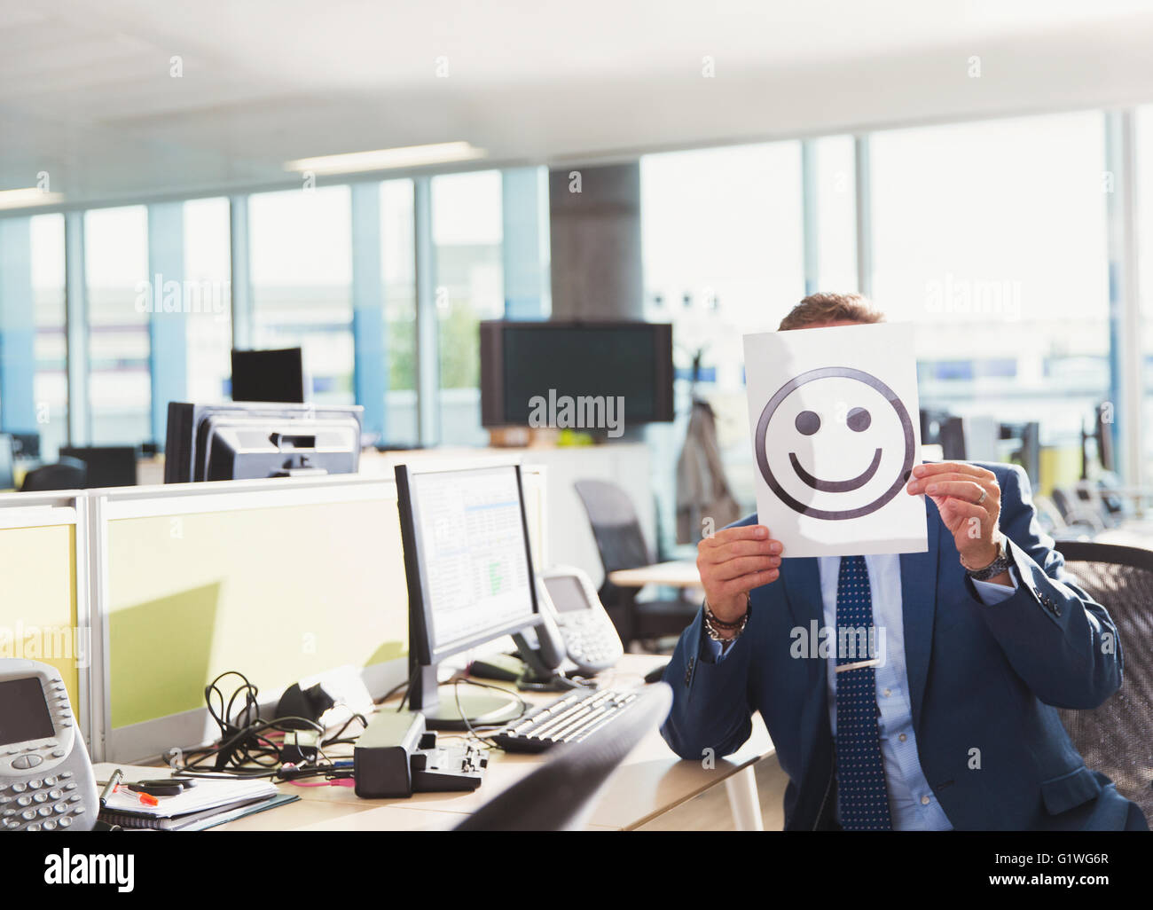 Portrait of businessman holding smiley face printout over his face in office Stock Photo