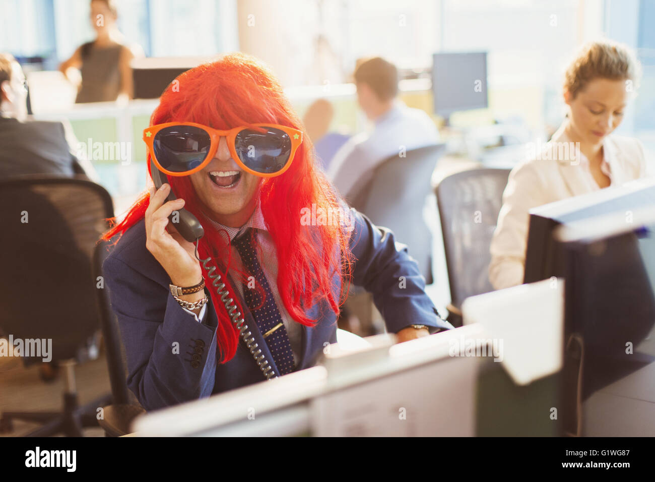 Portrait playful businessman wearing red wig and huge sunglasses in office Stock Photo