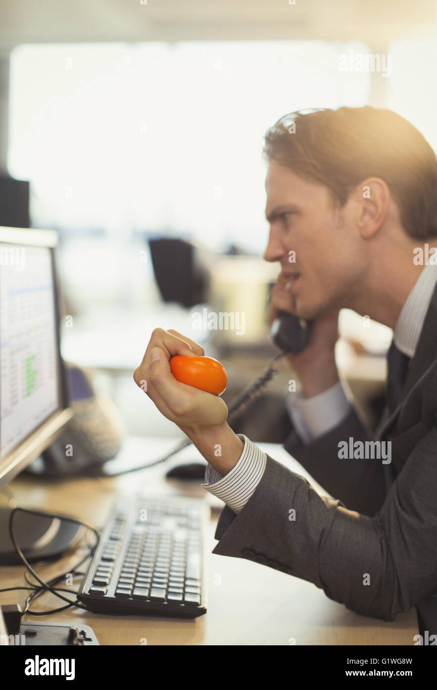 Angry businessman squeezing stress ball and talking on telephone at computer in office Stock Photo