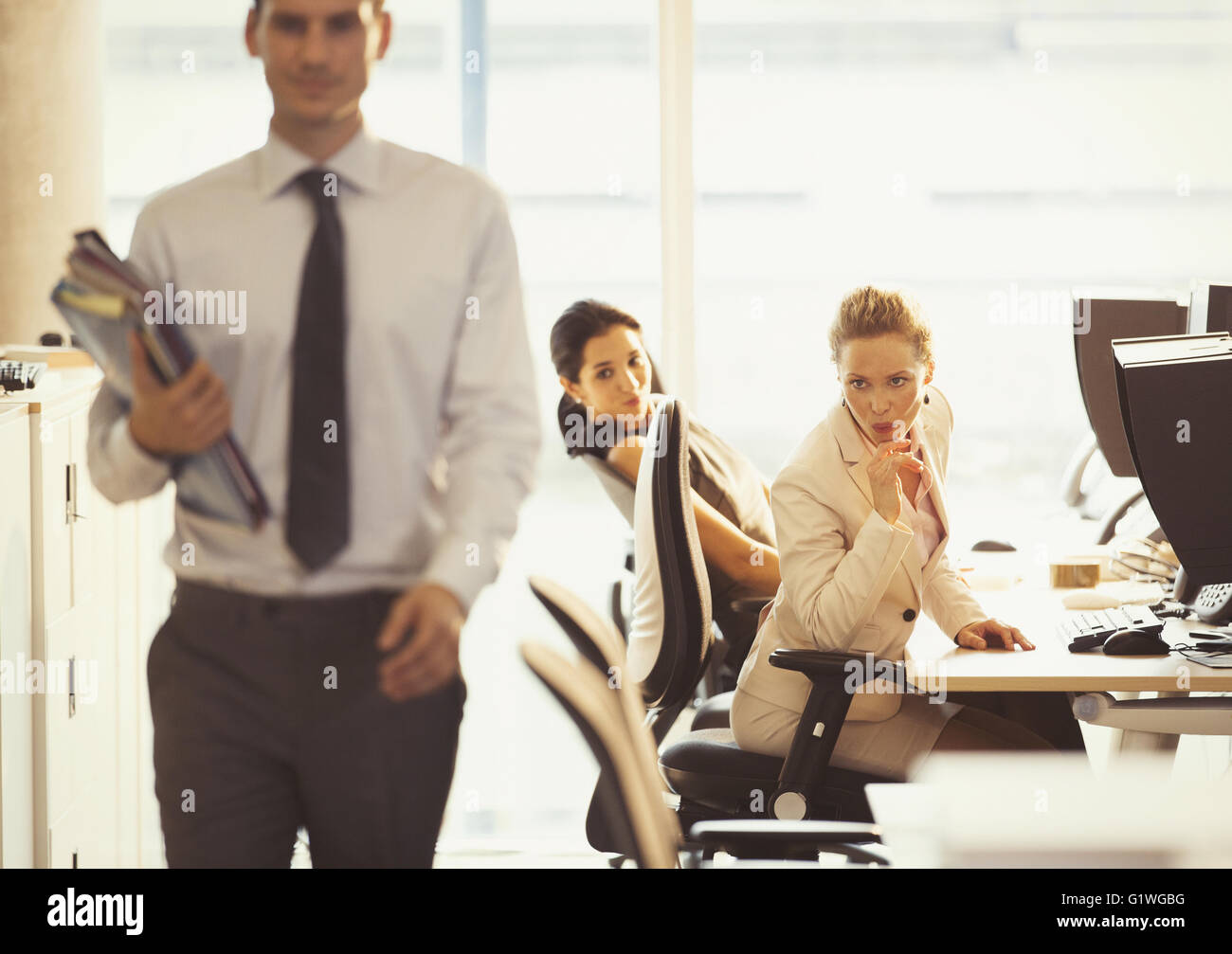 Businesswomen checking out passing businessman in office Stock Photo