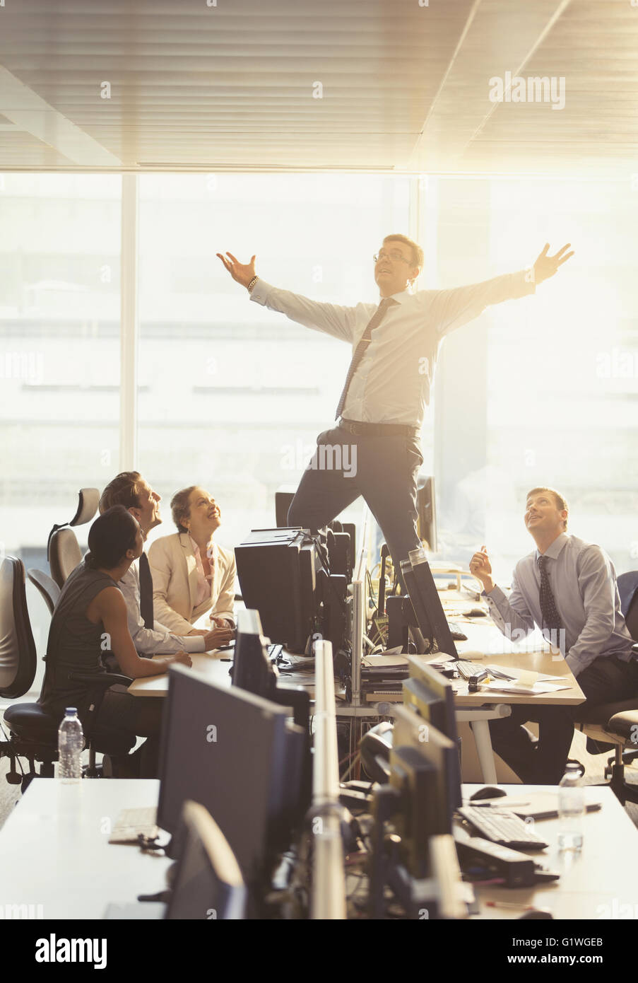 Colleagues watching exuberant businessman celebrating on top of desks in office Stock Photo