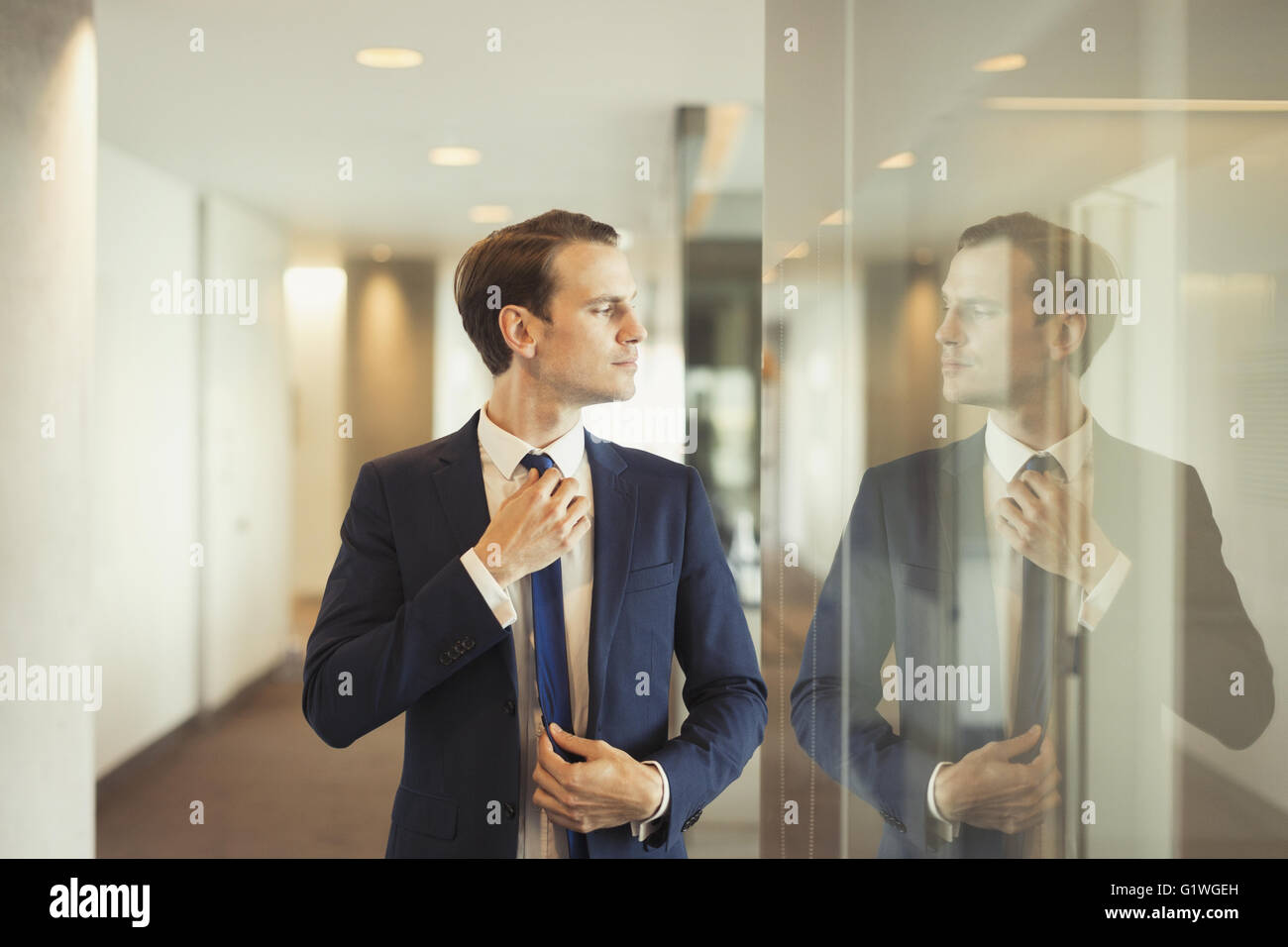 Confident businessman adjusting tie in office corridor Stock Photo