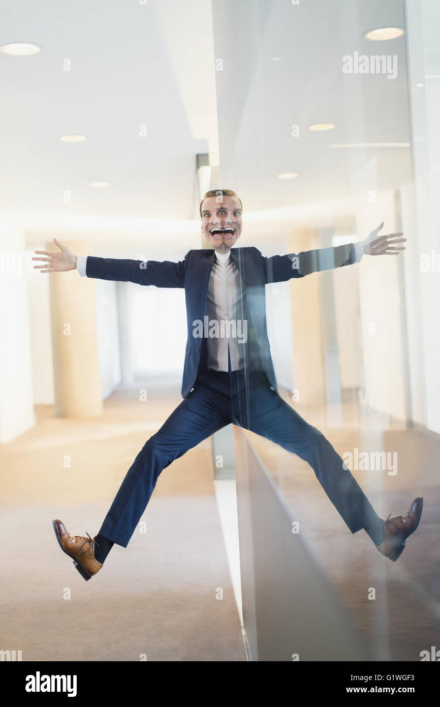 Symmetrical reflection portrait of businessman with arms and legs outstretched in office corridor Stock Photo