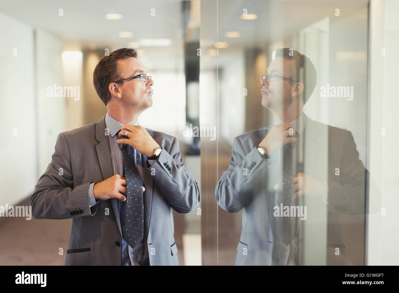 Reflection of confident businessman adjusting tie in office corridor Stock Photo