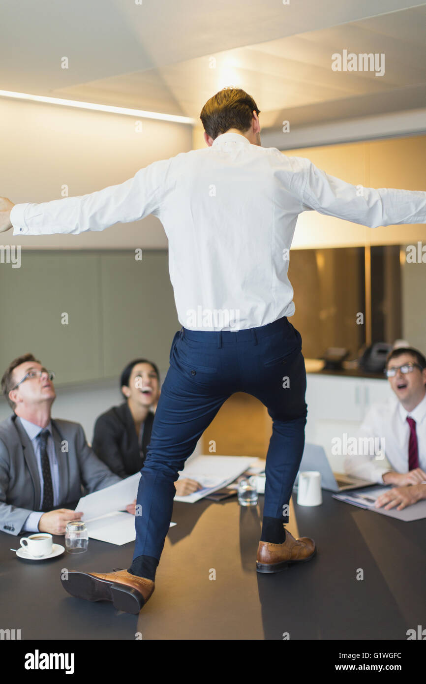 Surprised colleagues watching exuberant businessman dancing on conference table Stock Photo