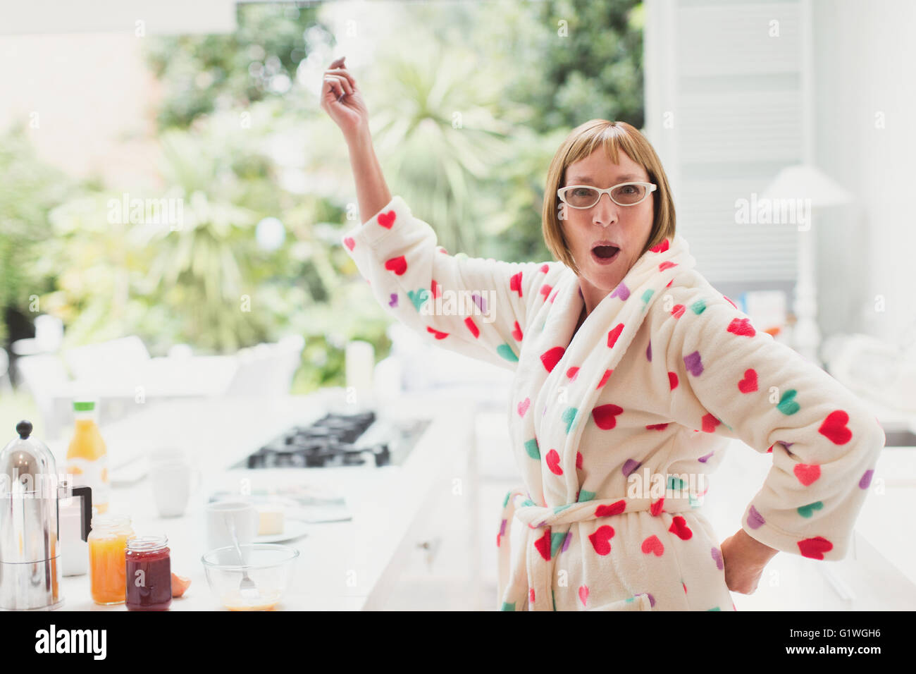 Portrait of playful mature woman in bathrobe dancing in kitchen Stock Photo