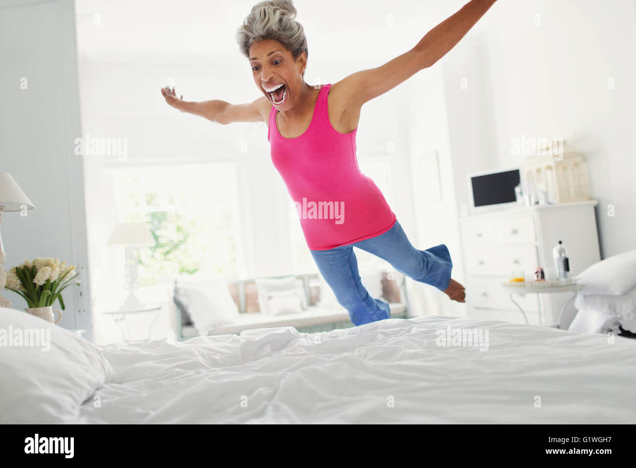 Playful mature woman jumping onto bed Stock Photo
