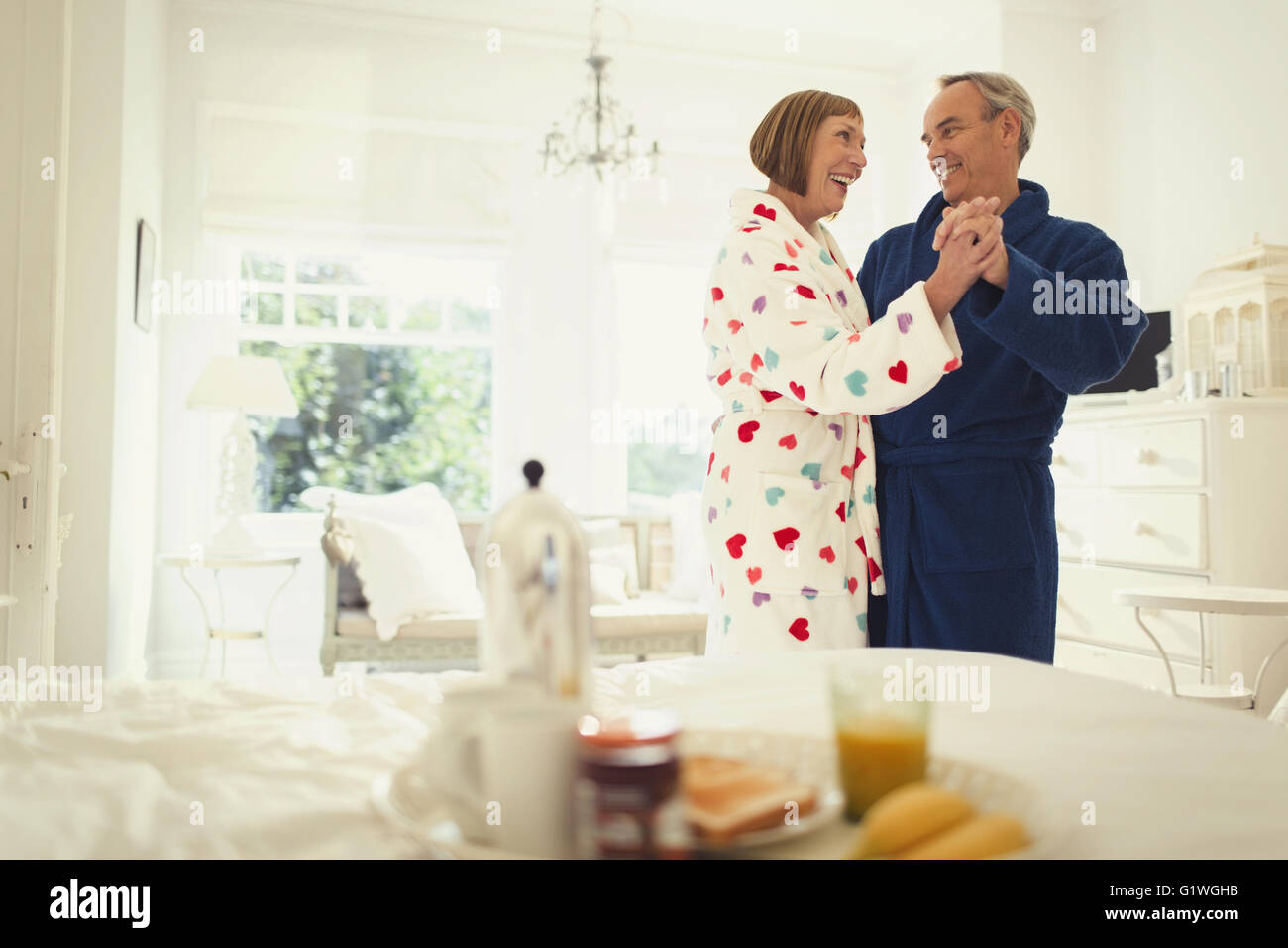 Mature couple dancing in bathrobes in bedroom Stock Photo